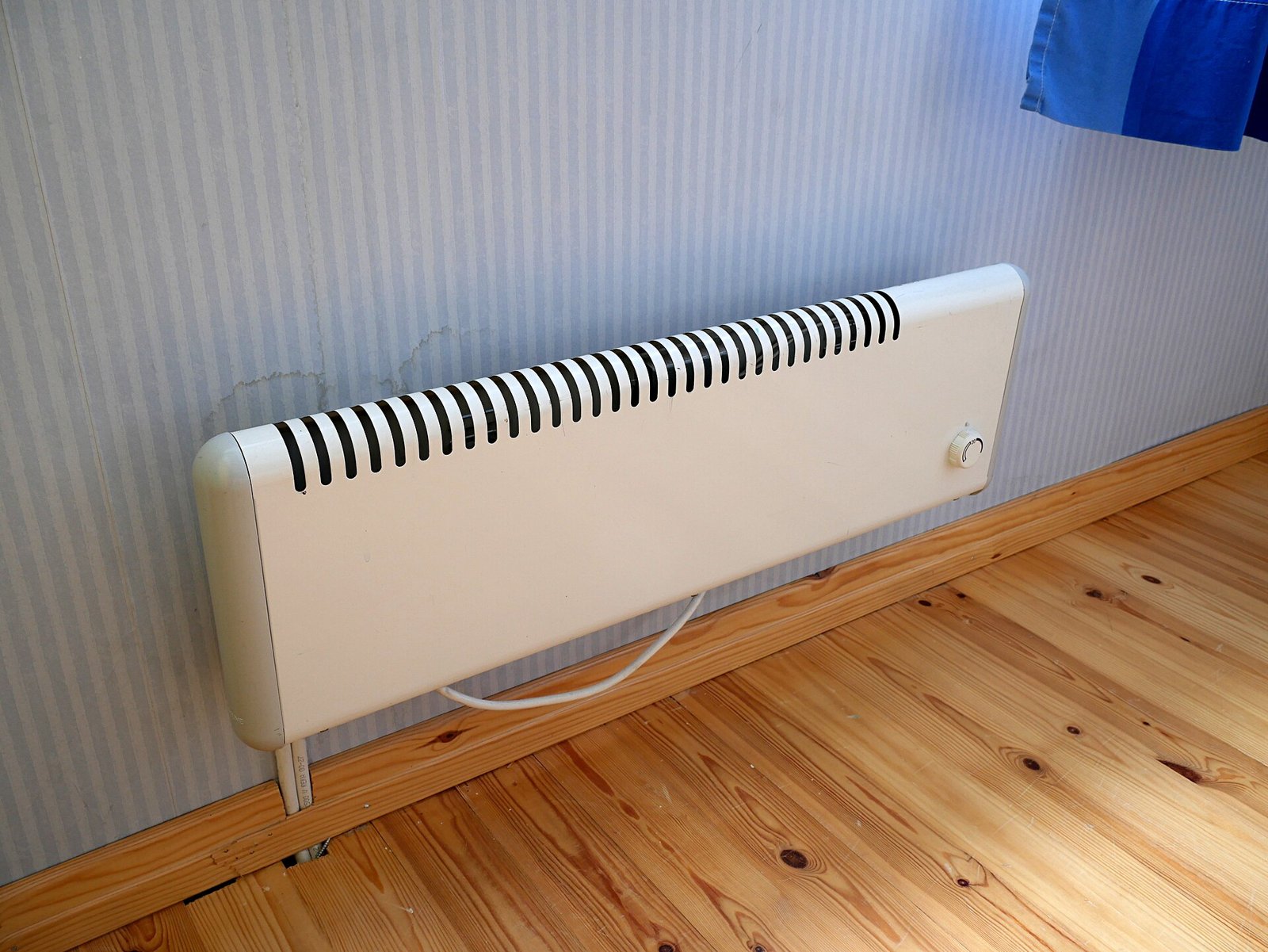 Radiateur électrique blanc fixé au bas d'un mur au-dessus d'un parquet clair