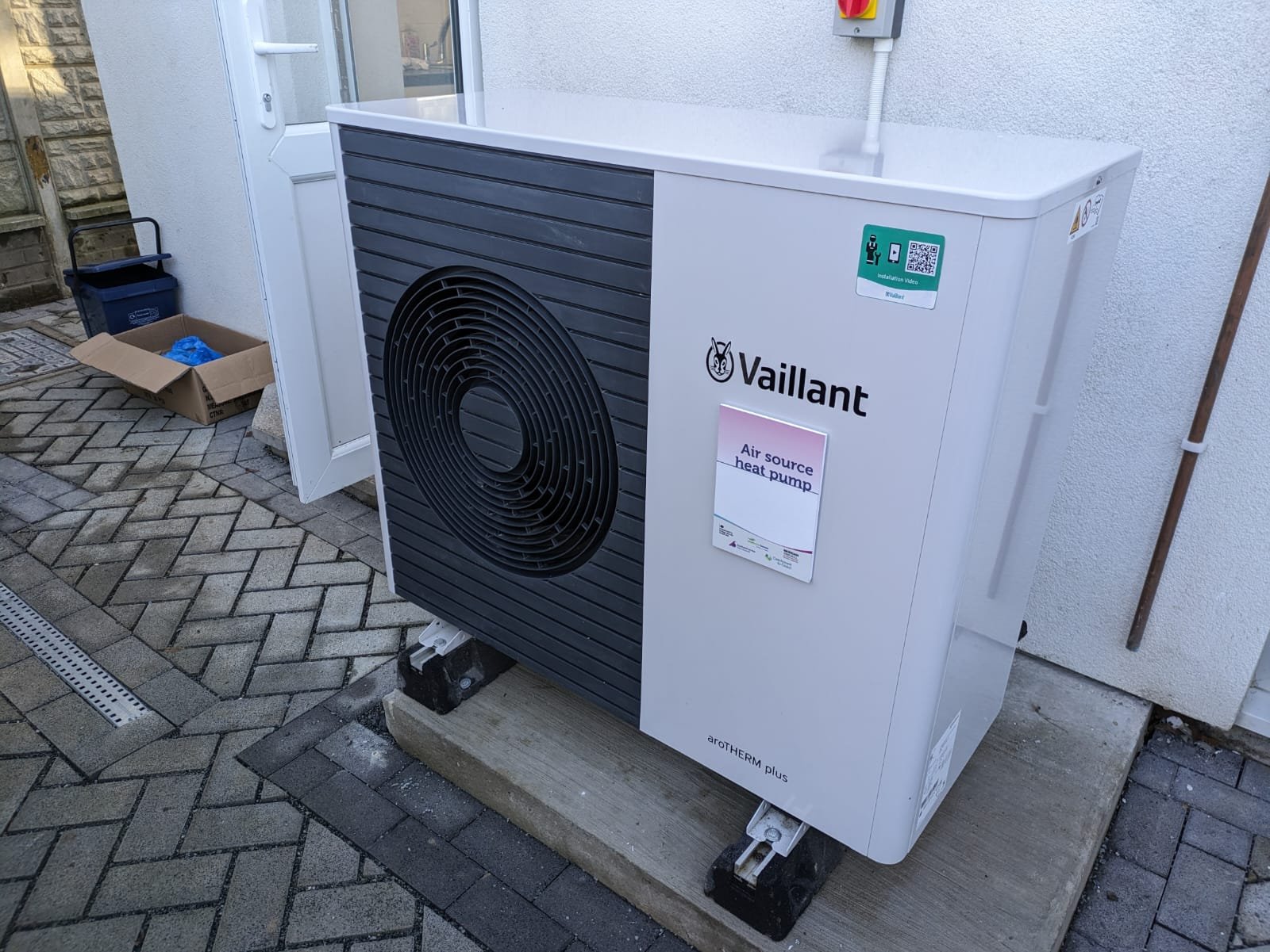 Unité extérieure blanche d'une pompe à chaleur air-eau installée au pied d'une maison