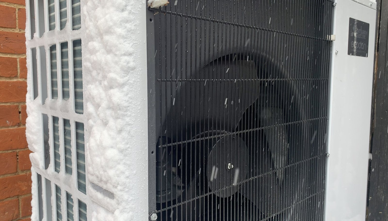 Unité extérieure de pompe à chaleur air-eau sous la neige contre le mur d'une maison